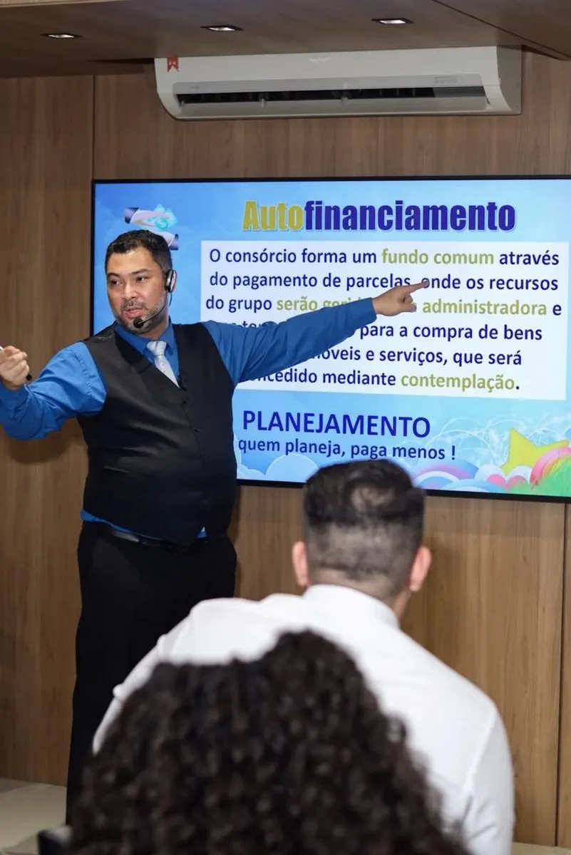 Clayton explicando autofinanciamento de consórcio, apontando para o slide projetado.