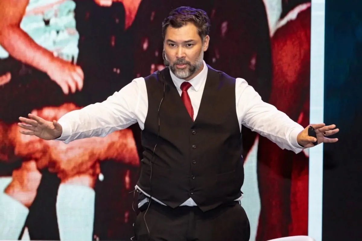 Clayton de colete e gravata vermelha abrindo os braços para a plateia no palco.