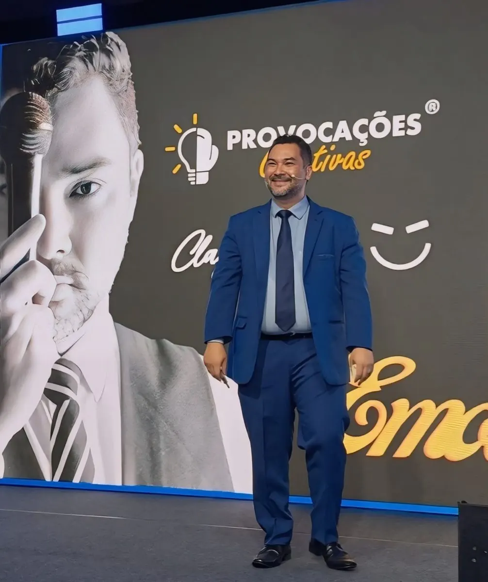 Clayton de terno azul no palco da Provocações Criativas, com o painel da marca ao fundo.