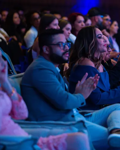 Plateia de um congresso corporativo rindo e aplaudindo nas poltronas.