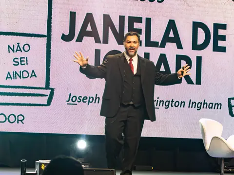 Clayton Yaso de braços abertos no palco, diante do slide “Janela de Johari”.