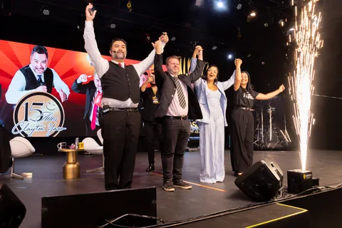 Encerramento de evento: Clayton Yaso e convidados com os braços erguidos no palco, com chuva de faíscas.