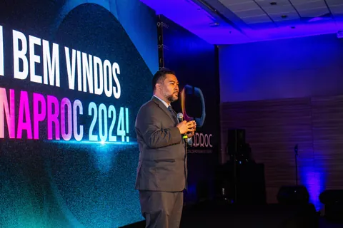 Clayton Yaso ao microfone diante do telão “Bem-vindos CONAPROC 2024!”.