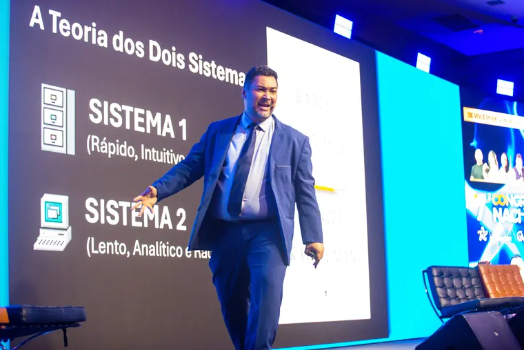 Clayton Yaso no palco diante do telão “A Teoria dos Dois Sistemas”, explicando o Sistema 1 e o Sistema 2.